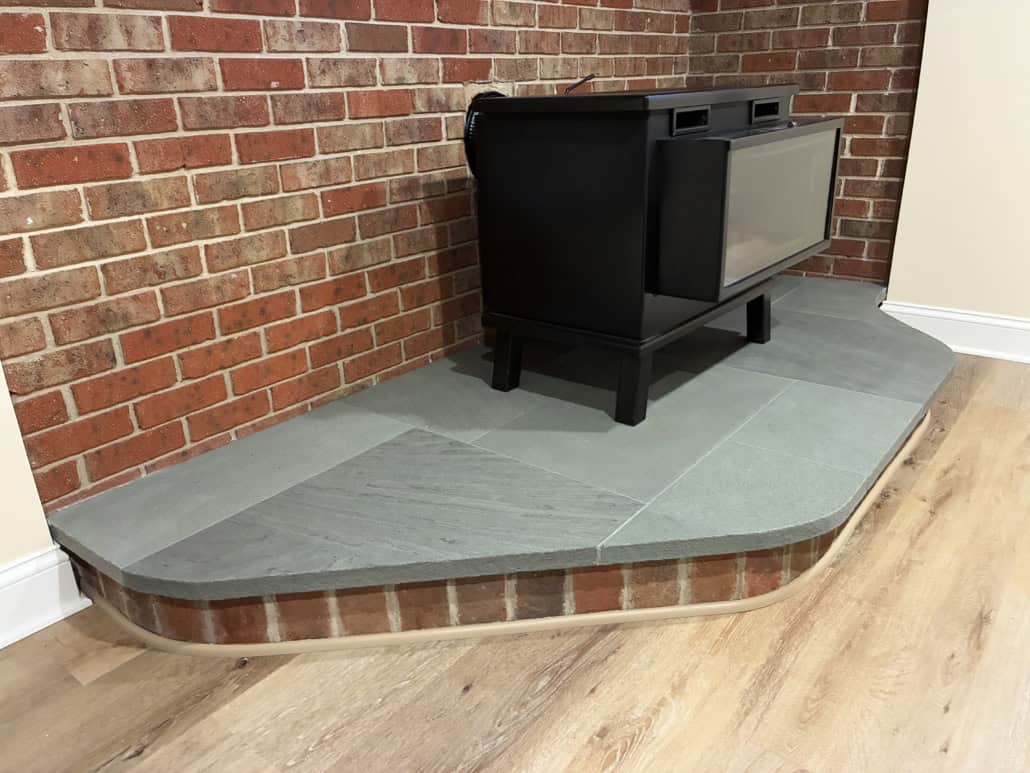 Custom-cut thermal bluestone hearth supporting a black wood stove against a rustic brick wall.