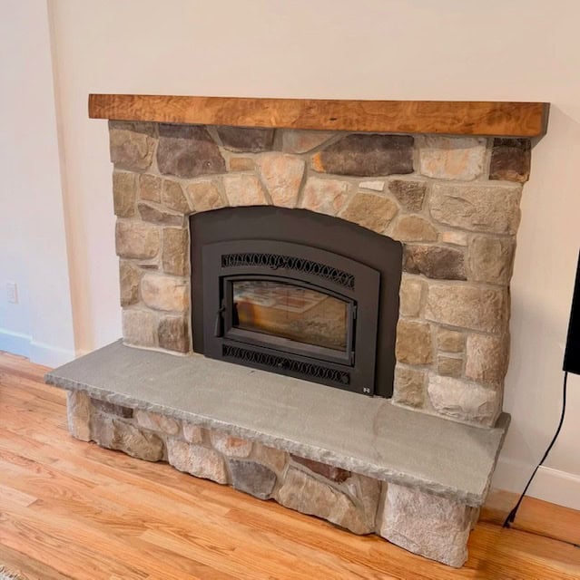 Natural stone fireplace featuring a rustic wood mantel and a grey bluestone hearth.