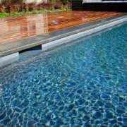 Modern swimming pool featuring grey bluestone coping with a half bullnose edge adjacent to a polished warm-toned wood deck.