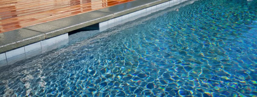 Modern swimming pool featuring grey bluestone coping with a half bullnose edge adjacent to a polished warm-toned wood deck.