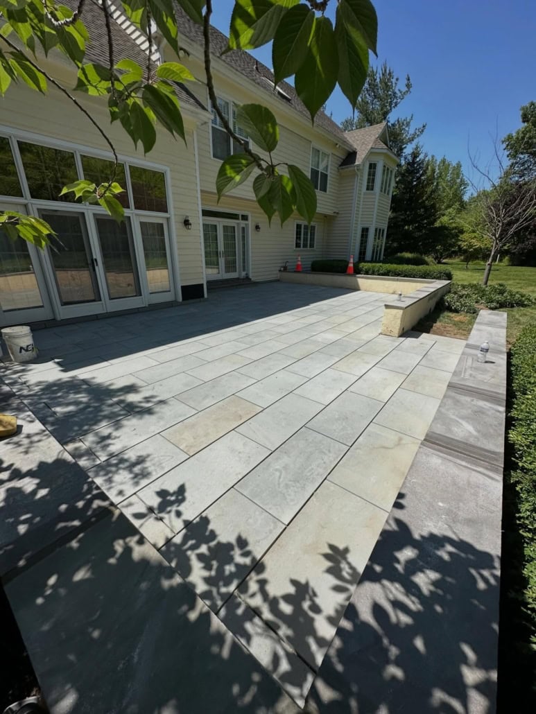Large residential patio featuring thermal bluestone pavers in a running bond pattern with a matching low retaining wall.