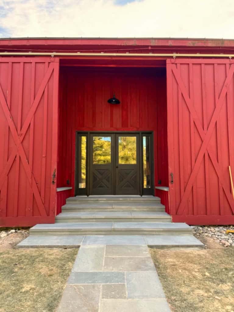 Thermal bluestone steps and risers leading to a modern red barn entryway with dark double doors and a matching stone walkway.