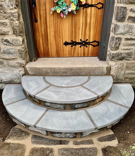 Custom-built semi-circular bluestone steps and landing with natural stone risers leading up to a wooden front door.
