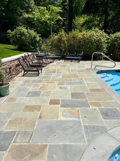 Custom flagstone pool deck with natural pattern bluestone pavers, stone retaining wall, and patio furniture.