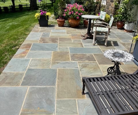 Full color natural cleft Pennsylvania bluestone patio arranged in a random pattern layout alongside a stone house.