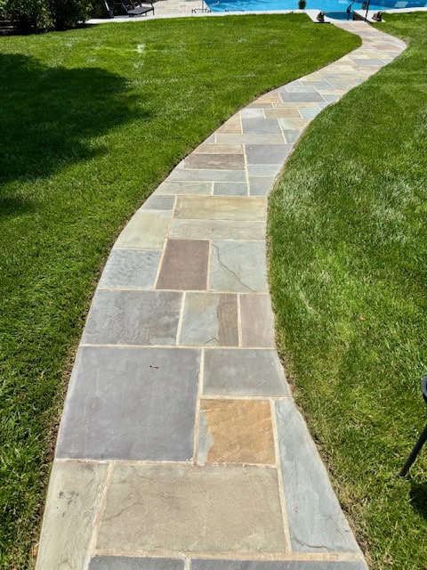 Full color natural cleft Pennsylvania bluestone walkway installed in a pattern design through a green lawn.