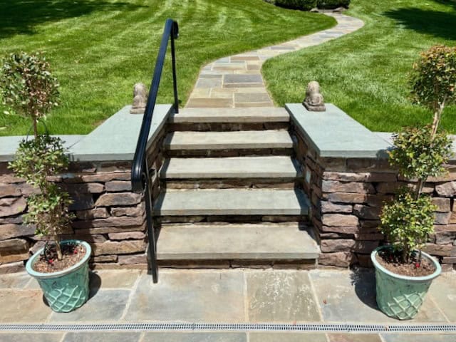 Thermal Pennsylvania bluestone step treads and matching wall caps on a natural stone retaining wall leading to a walkway.