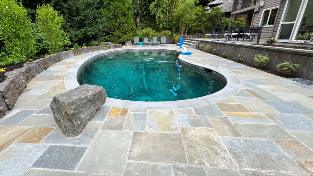 Natural cleft flagstone pool deck with custom bluestone coping, large landscape accent boulder, and custom freeform pool.