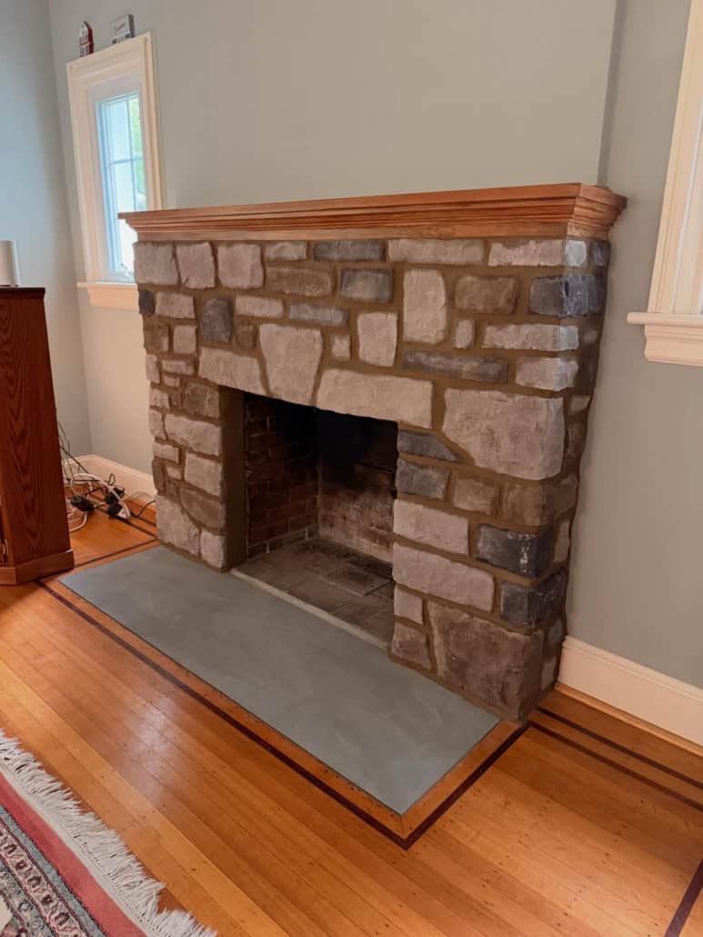 Traditional stone fireplace featuring a flush bluestone hearth slab and warm wooden mantel.