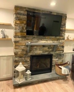 Stacked earth-tone stone fireplace with gray bluestone mantel and low hearth slab.