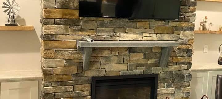 Stacked earth-tone stone fireplace with gray bluestone mantel and low hearth slab.