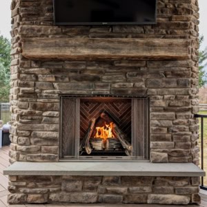 Stacked stone outdoor fireplace featuring a rustic timber mantel and bluestone hearth.
