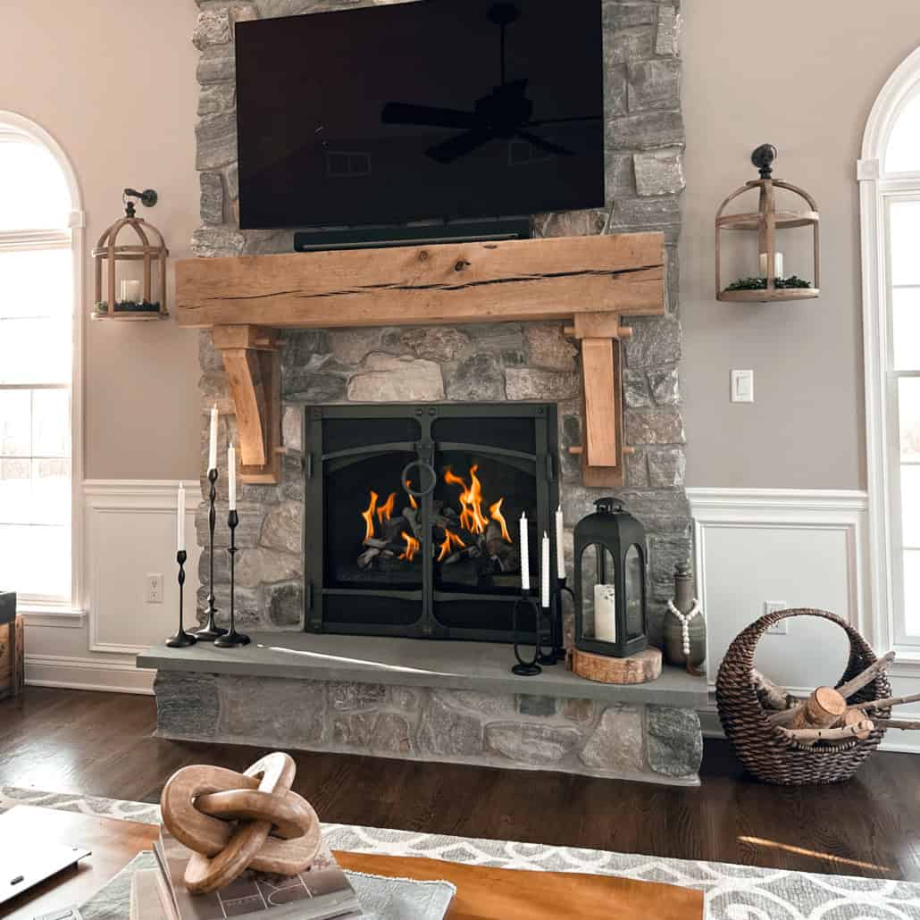 Stacked stone fireplace with a thick rustic wood mantel, bluestone hearth, and mounted TV