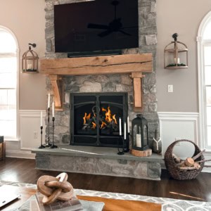 Stacked stone fireplace with a thick rustic wood mantel, bluestone hearth, and mounted TV