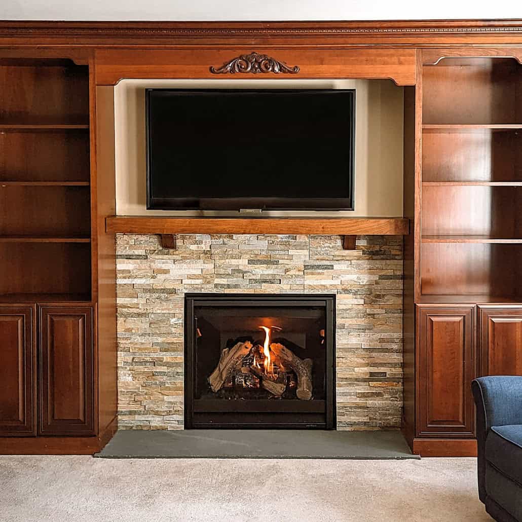 Stacked stone fireplace insert with floor-flush bluestone hearth surrounded by custom cherry built-in cabinets.