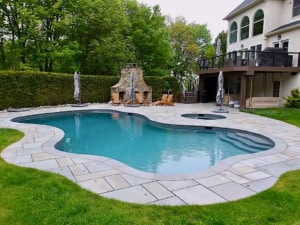 Custom full-bullnose bluestone pool coping edging a freeform swimming pool with a variegated thermal bluestone paver patio.